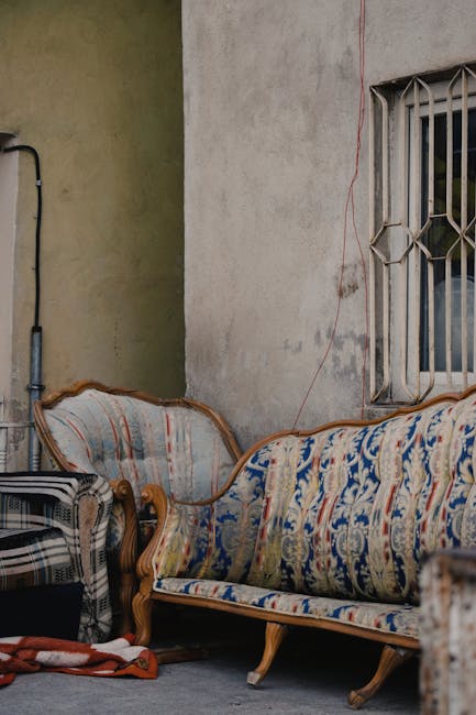 A vintage brown upholstered sofa with wooden frame and armrests positioned in front of a large, densely packed wall of mixed waste and recyclable materials, including crumpled cardboard boxes, shredde