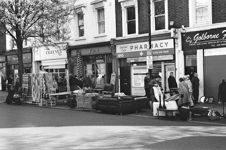 In front of a traditional brick-fronted building housing a bar and restaurant, there is a black commercial waste bin positioned on the sidewalk. The bin has a slightly open lid with cardboard boxes an
